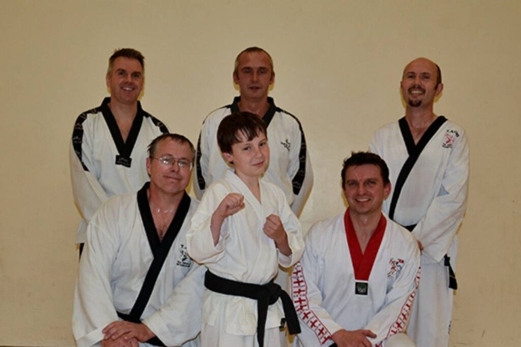 A group photo of martial arts instructors and young students in traditional uniforms, smiling.
